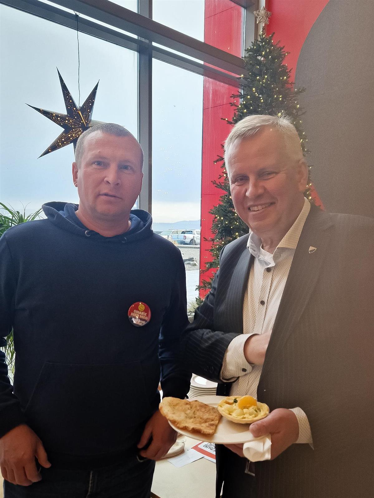 Bilde av en elev fra kvalifiseringsenheten og Ordfører Hallgeir Grøntvedt som holder et fat med mat på. I bakgrunnen ser man julestjerne i et vindu og pyntet juletre. - Klikk for stort bilde