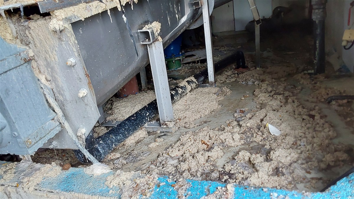 Et anlegg dekket av lyst, klumpete materiale. Det ligger tilsvarende materiale spredt på betonggulvet rundt anlegget. - Klikk for stort bilde
